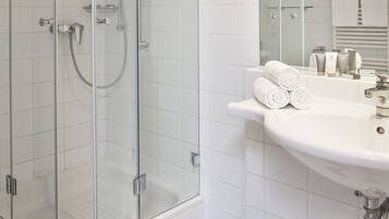 A bathroom with a glass-enclosed shower, white tiles, a sink with toiletries, and a checkered floor.