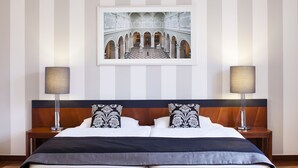 A hotel room with a large bed, two bedside tables with lamps, a framed picture on the wall, and a striped wall design. - Hapimag Resort Budapest (Budapest)