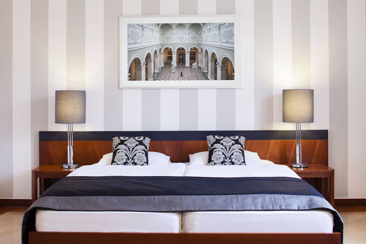 Habitación de hotel con una cama grande, dos mesitas de noche con lámparas, un cuadro en la pared y un diseño de pared a rayas.