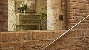 A rustic brick wall with a wooden dresser and a mirror reflecting a vase of flowers. - Hapimag Resort Budapest (Budapest)