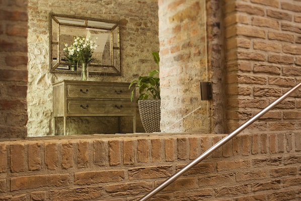 A rustic brick wall with a wooden dresser and a mirror reflecting a vase of flowers. - Hapimag Resort Budapest (Budapest)