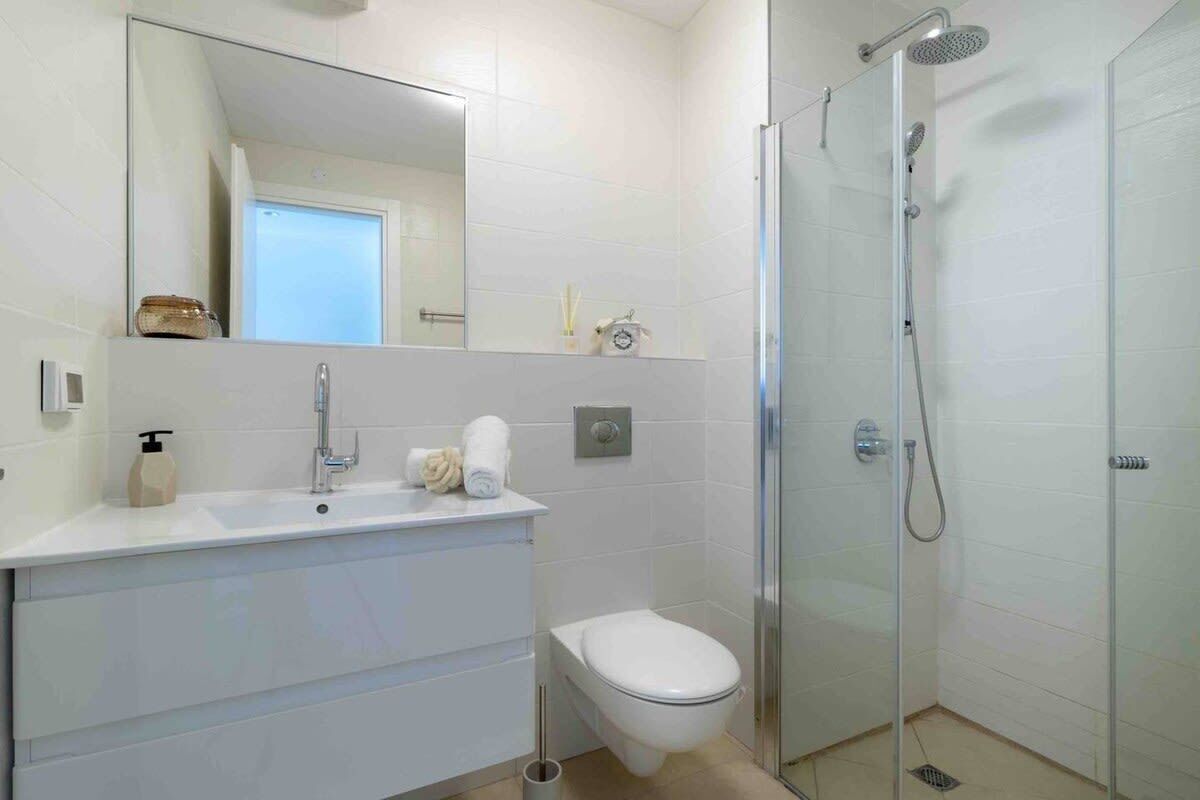 Et moderne badeværelse med hvid vask, toilet og brusebad med glasvægge.