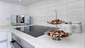 A modern kitchen with a built-in stove, a microwave, and a two-tiered serving tray with cookies. There are jars labeled "TEA" and "COFFEE" on the counter.