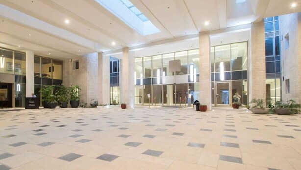 A spacious lobby with a high ceiling, large windows, and potted plants.