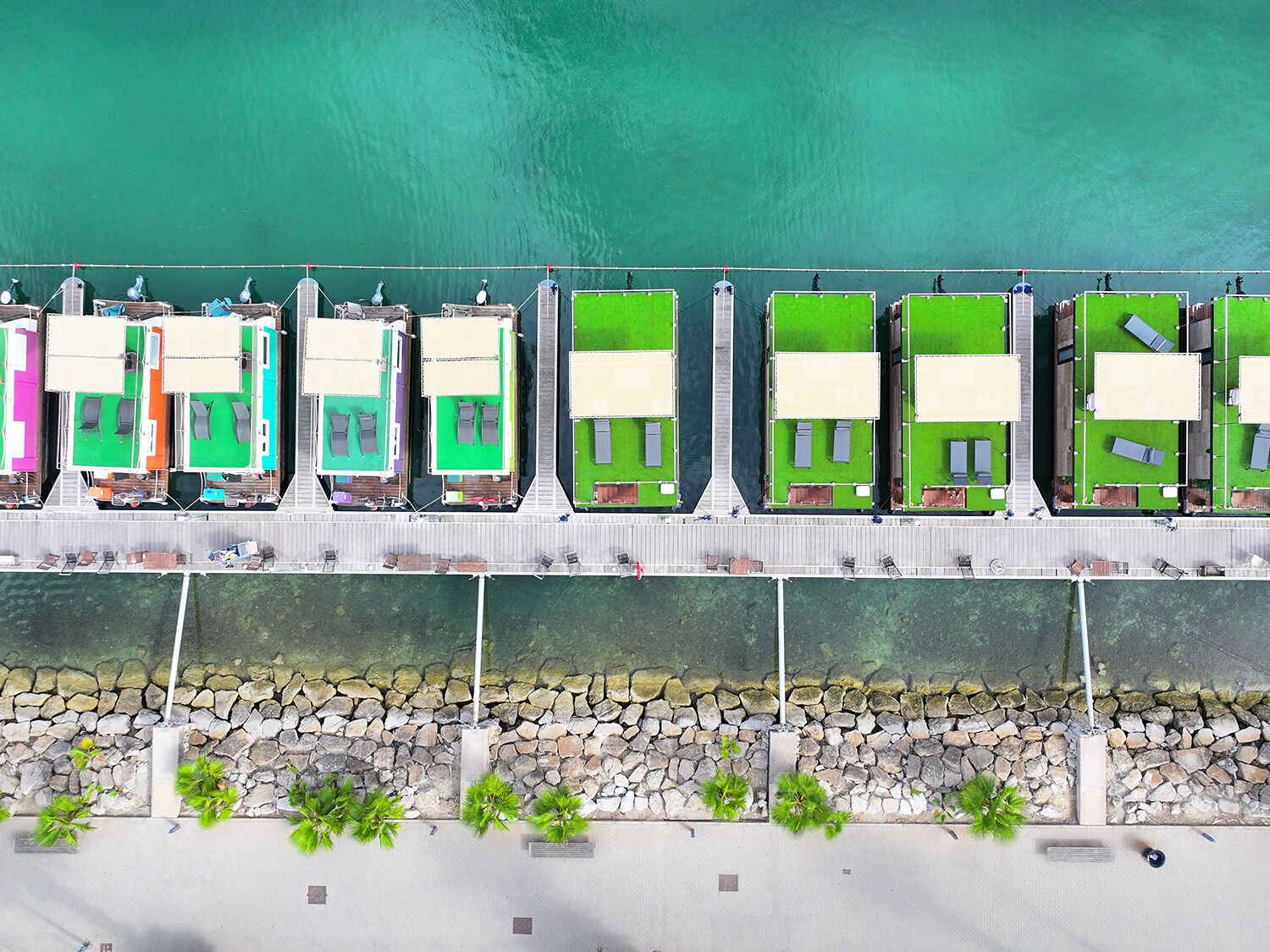 A row of colorful, rectangular, single-story buildings with green roofs, situated along a waterfront.