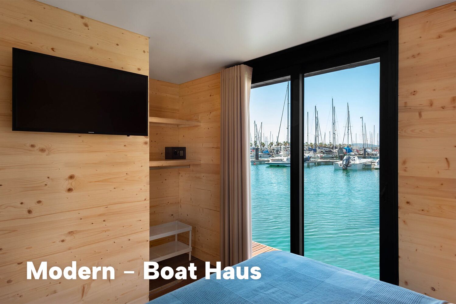 Ein modernes Bootshaus mit Wandfernseher, einer kleinen Sitzecke und Blick auf einen Yachthafen.