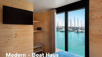 Una casa moderna para barcos con televisor en la pared, una zona de estar pequeña y vista a un puerto deportivo.