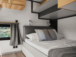 A compact bedroom with a bed, bedside lamps, a window with curtains, and a view of a body of water.