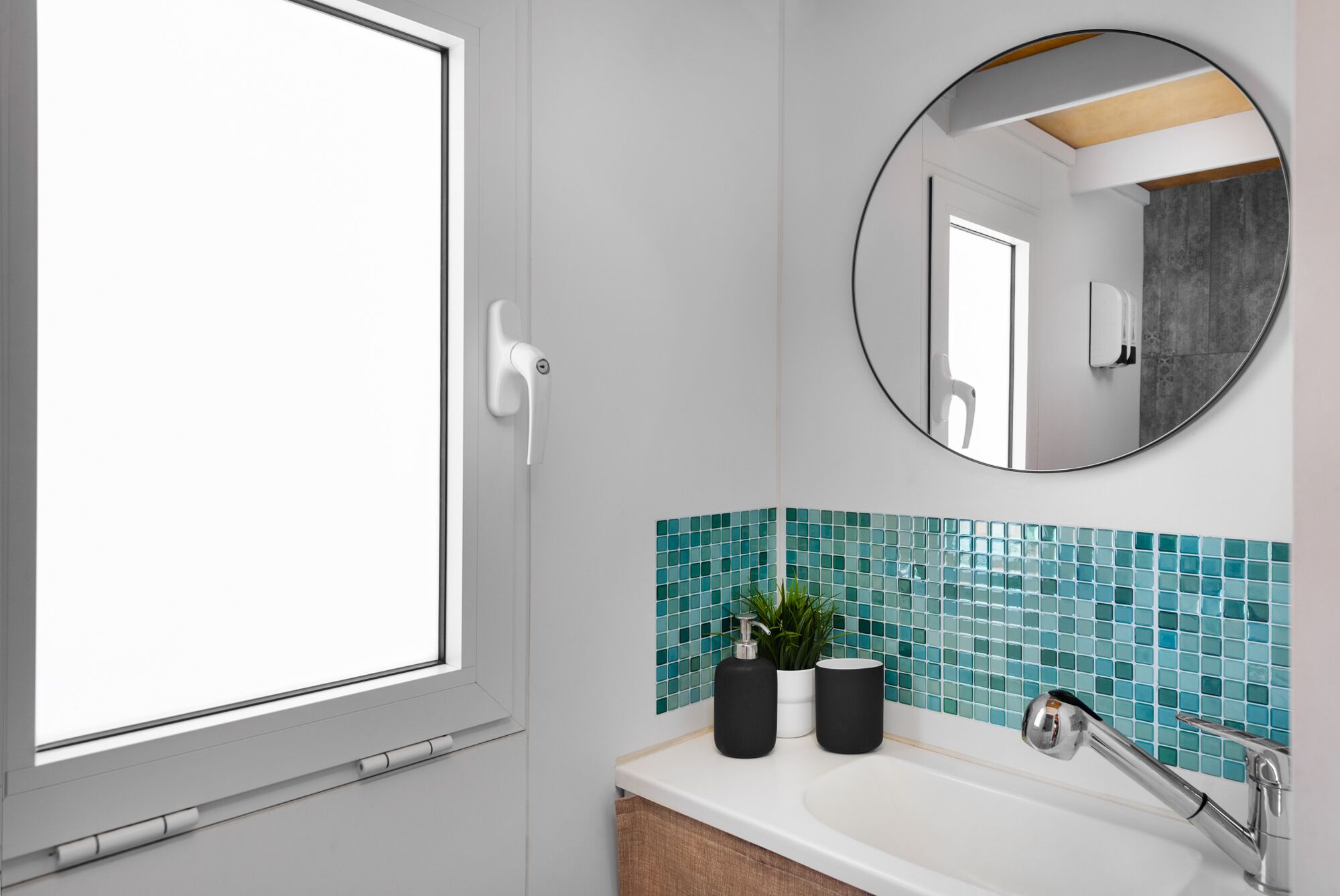 Un baño con ventana, lavamanos, espejo y salpicadero de azulejos.