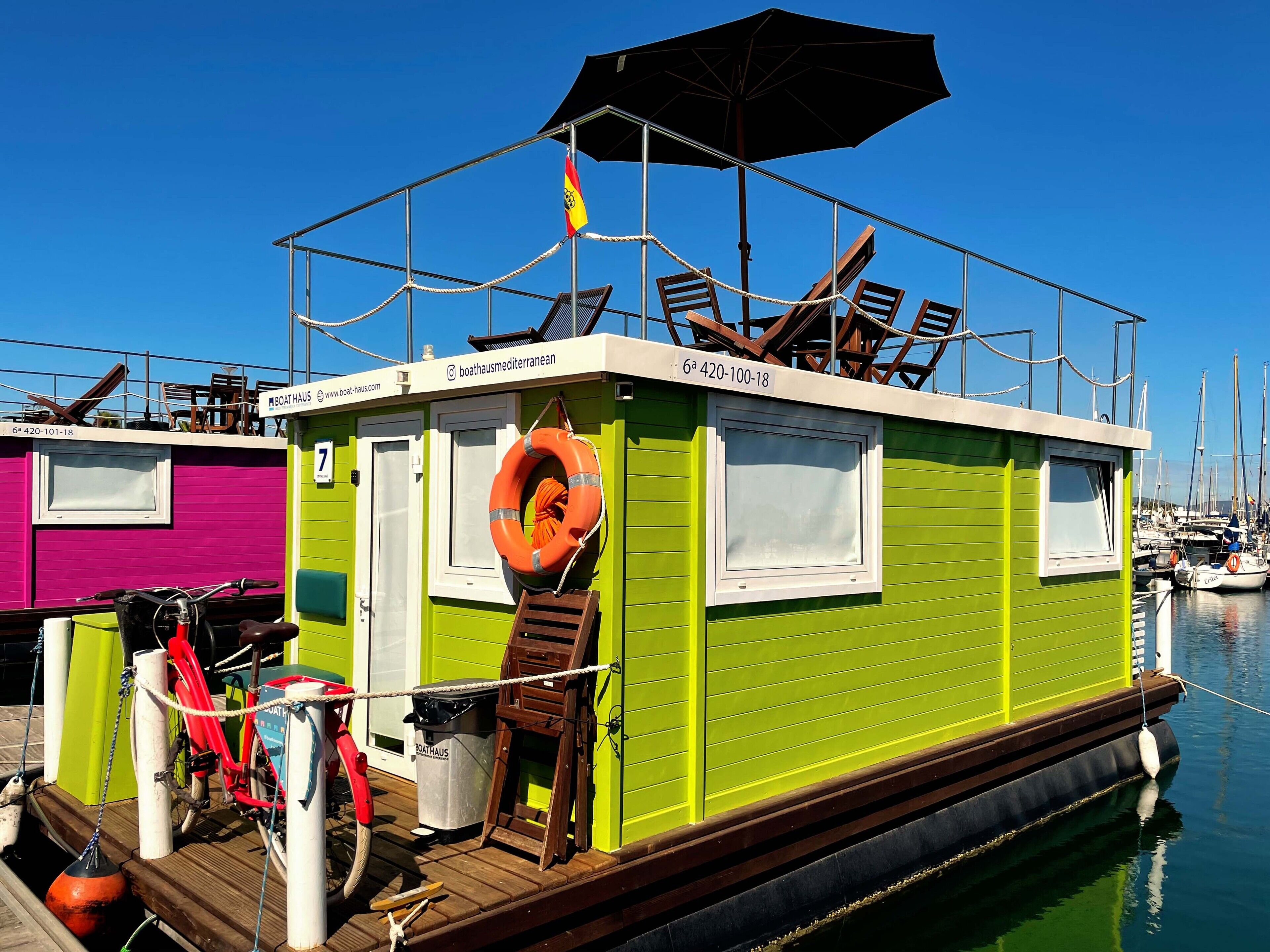 Um armazém de barcos verde com um círculo salva-vidas, uma bicicleta e uma pequena lixeira.