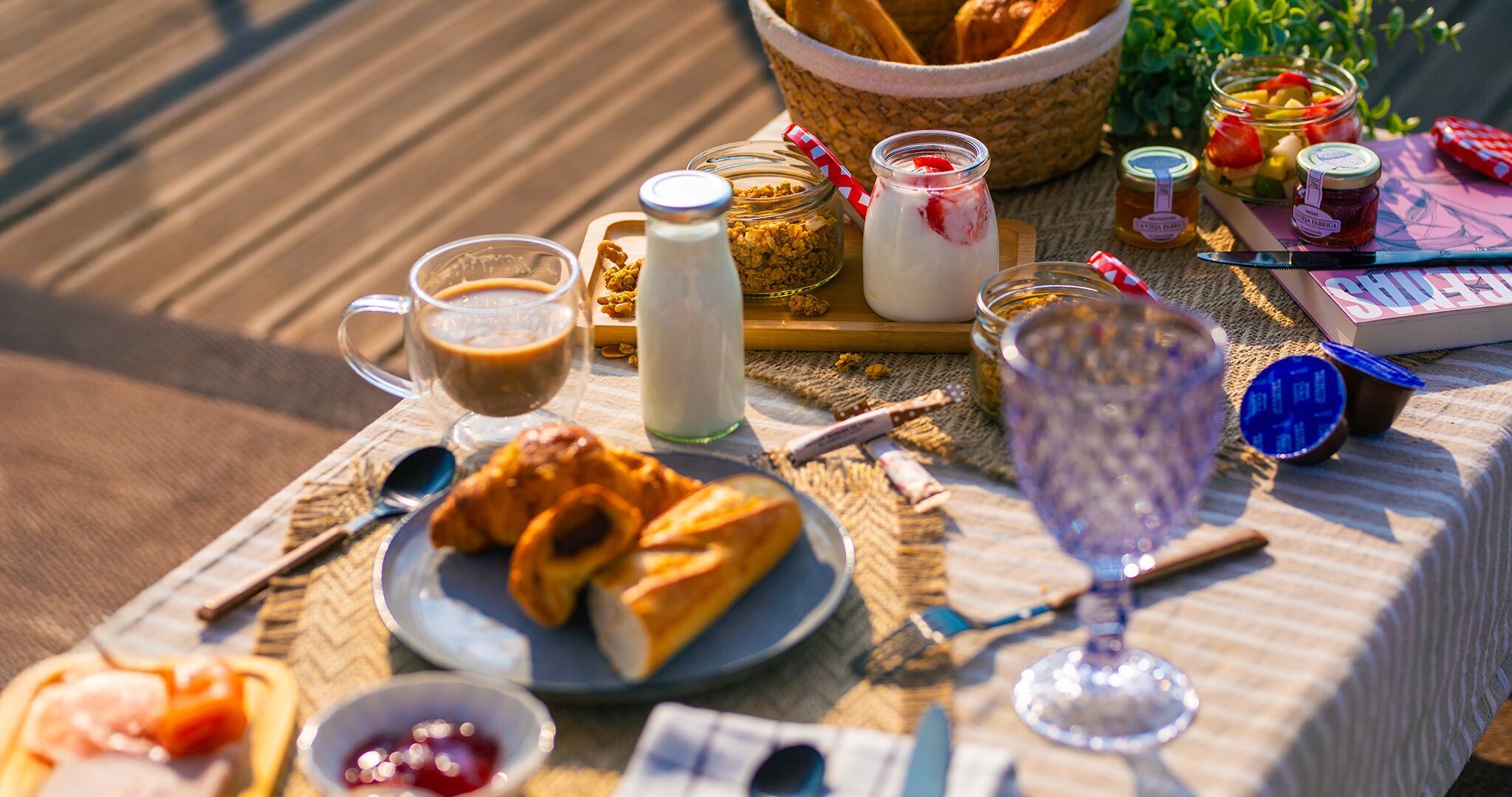 A breakfast setup with croissants, milk, jam, and a book on a table.