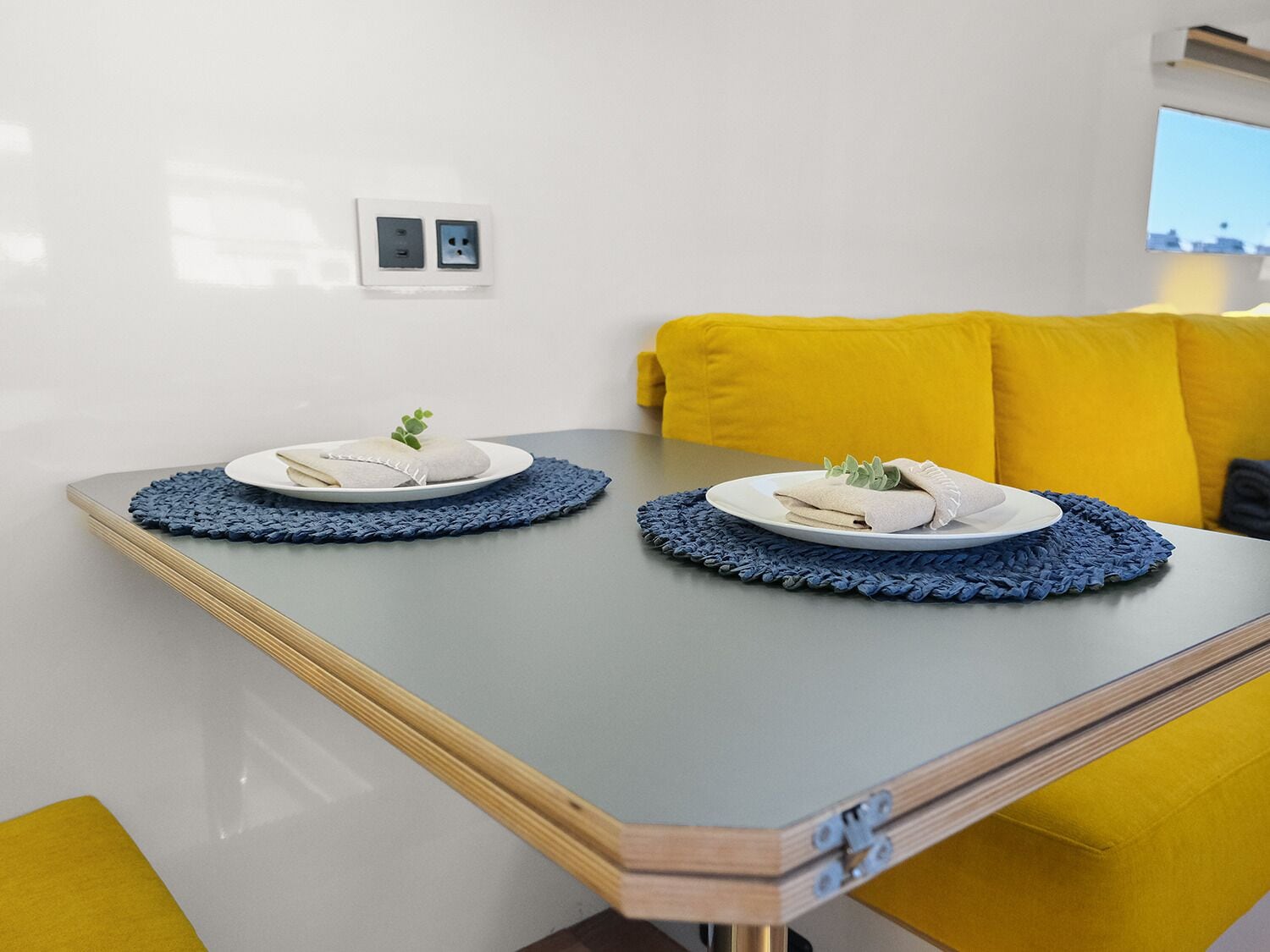 Una habitación moderna con una mesa para dos, un sofá amarillo y un aire acondicionado instalado en la pared.
