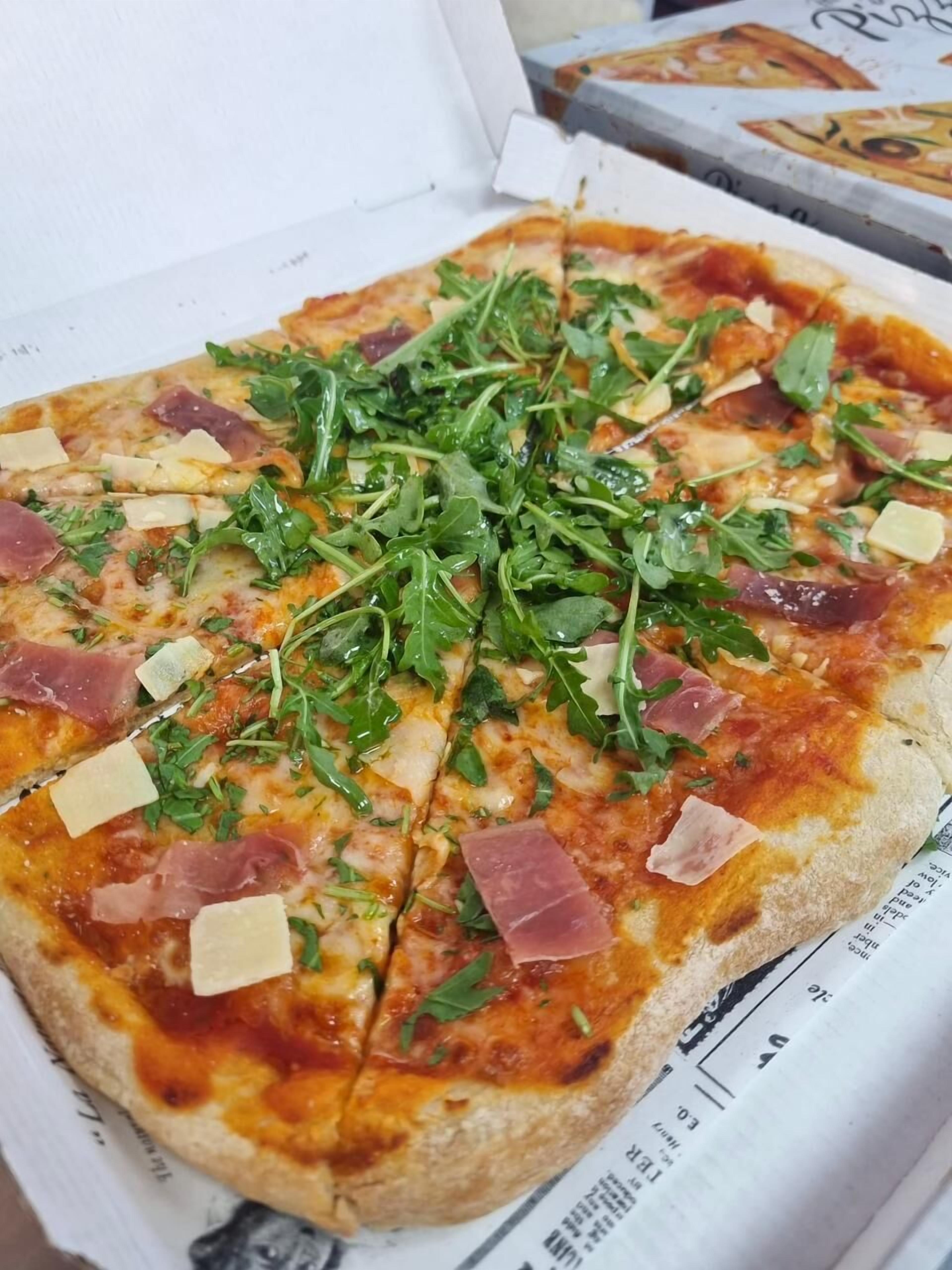 A pizza with arugula, cheese, and ham toppings.