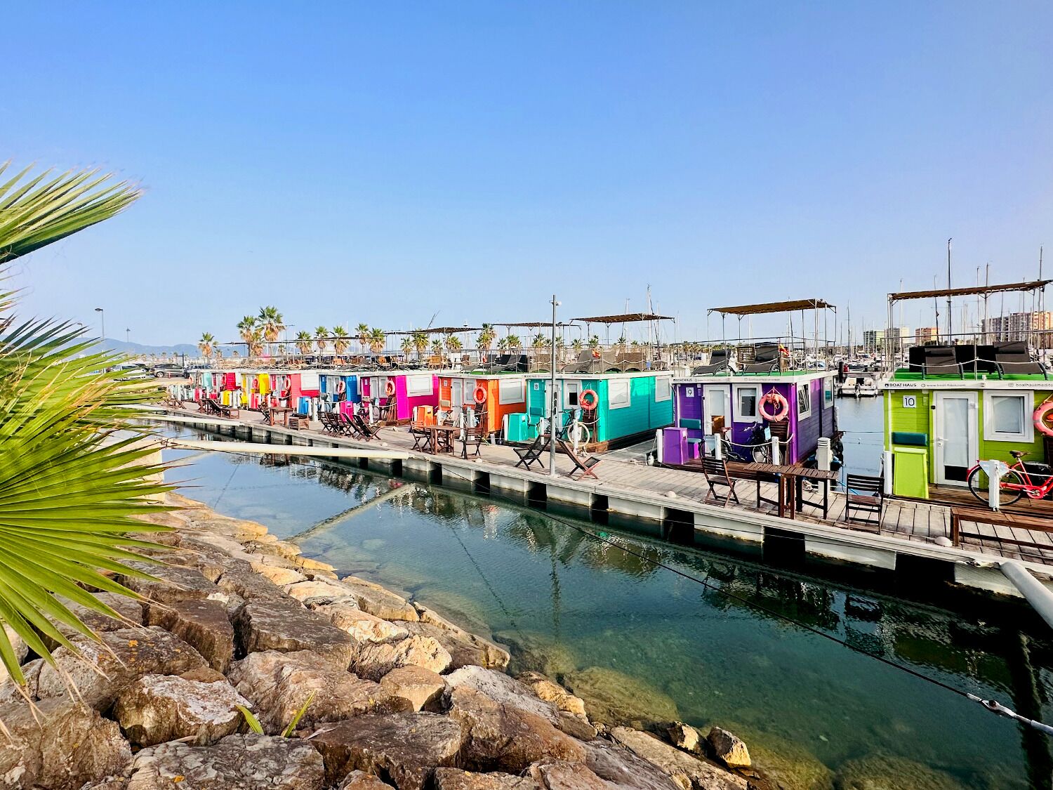 Filas de cabañas pequeñas y coloridas, con un muelle y puerto deportivo al fondo.