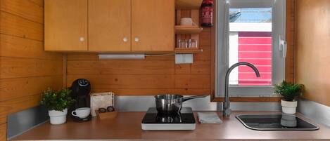A compact kitchen with wooden cabinets, a sink, a stove, and a window with a red blind.