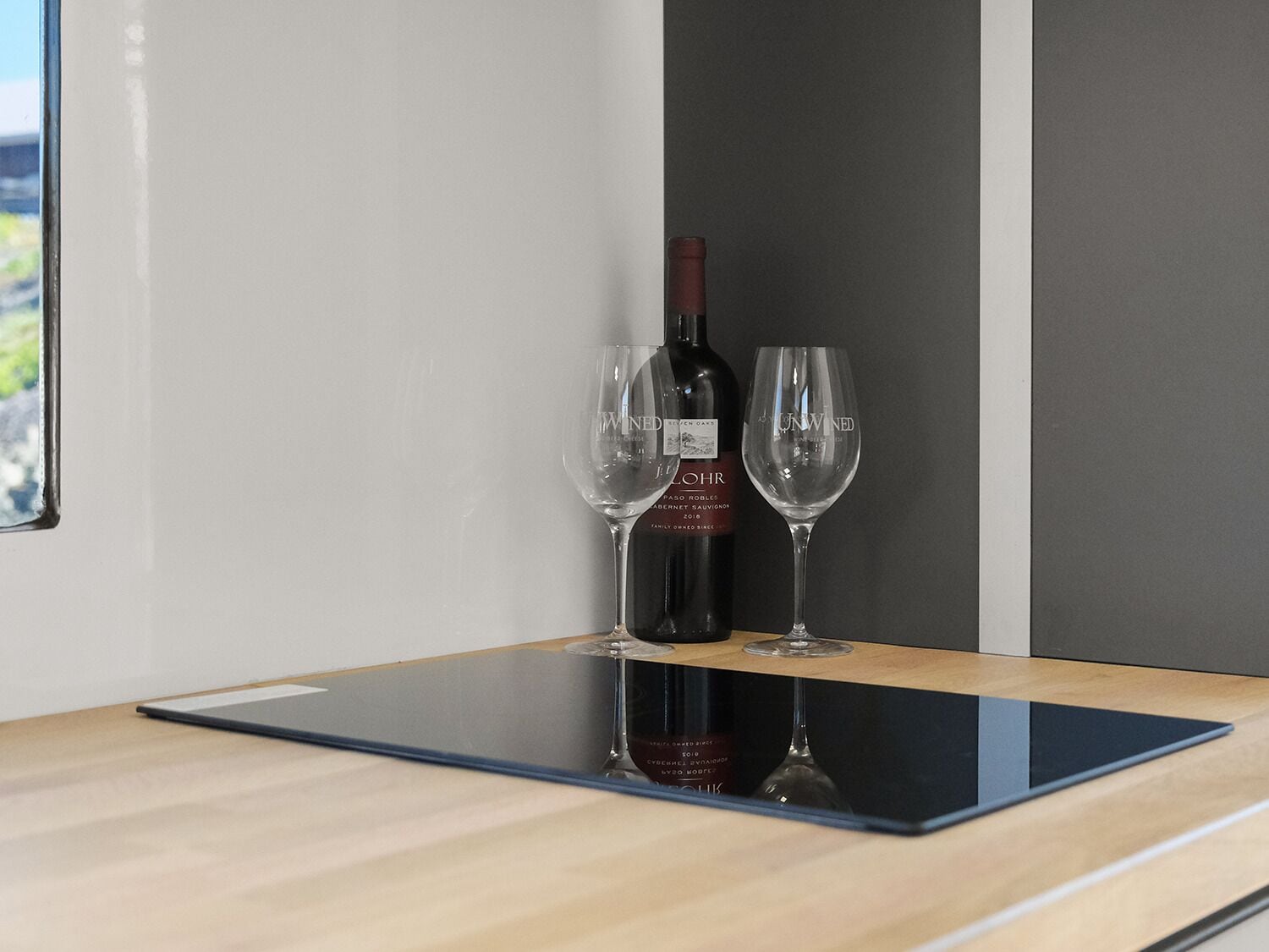 Una botella de vino y dos copas sobre una mesa de madera con superficie de vidrio.