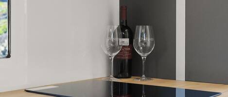 Una botella de vino y dos copas sobre una mesa de madera con superficie de vidrio.