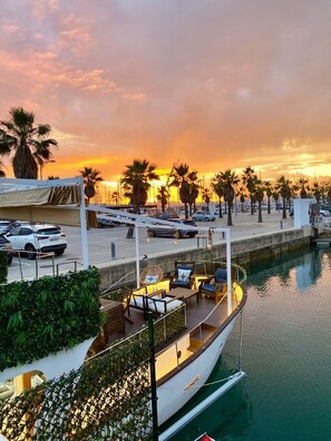 Un puerto deportivo con un barco amarrado, rodeado de palmeras y un atardecer de fondo.