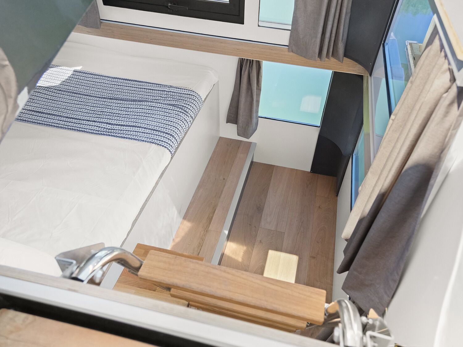 A compact, modern RV interior with a bed, a small table, and a window with curtains.
