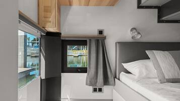 Una camera compatta e moderna con un letto, una piccola finestra vista su un corpo d'acqua e un angolo cottura.