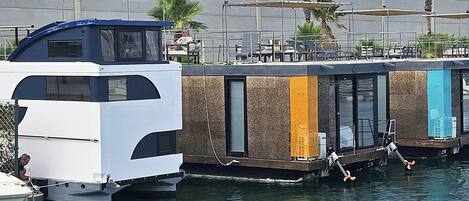 A houseboat docked at a marina with a covered deck area and a small boat nearby.