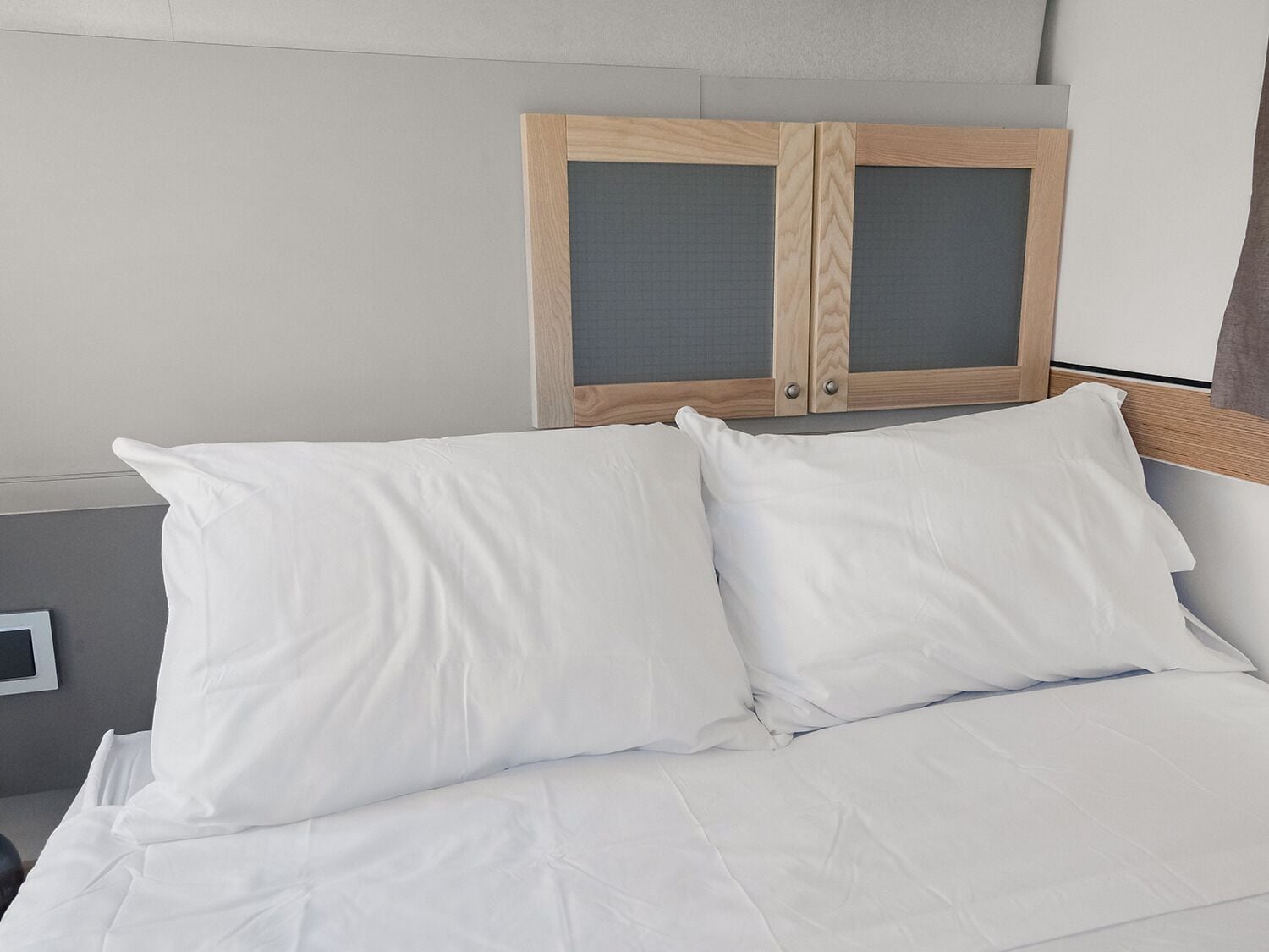 A bed with white bedding and a wooden headboard with two glass panels.