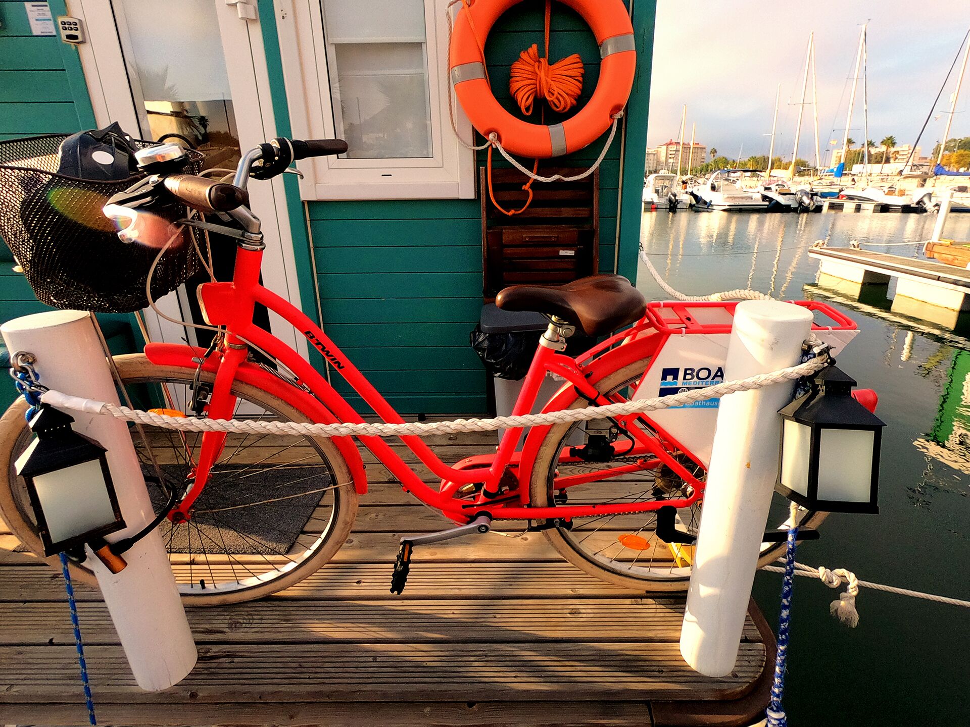 Una bicicleta roja atada a un muelle con una cuerda, un flotador salvavidas y un letrero que dice "BOA Mediterranean".