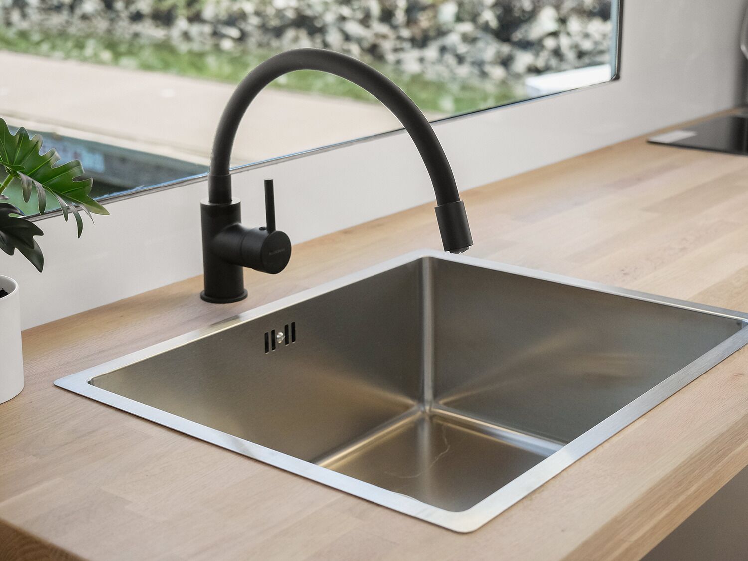 Une cuisine moderne avec un évier en acier inoxydable, un robinet noir et une plante en pot posée sur le plan de travail.