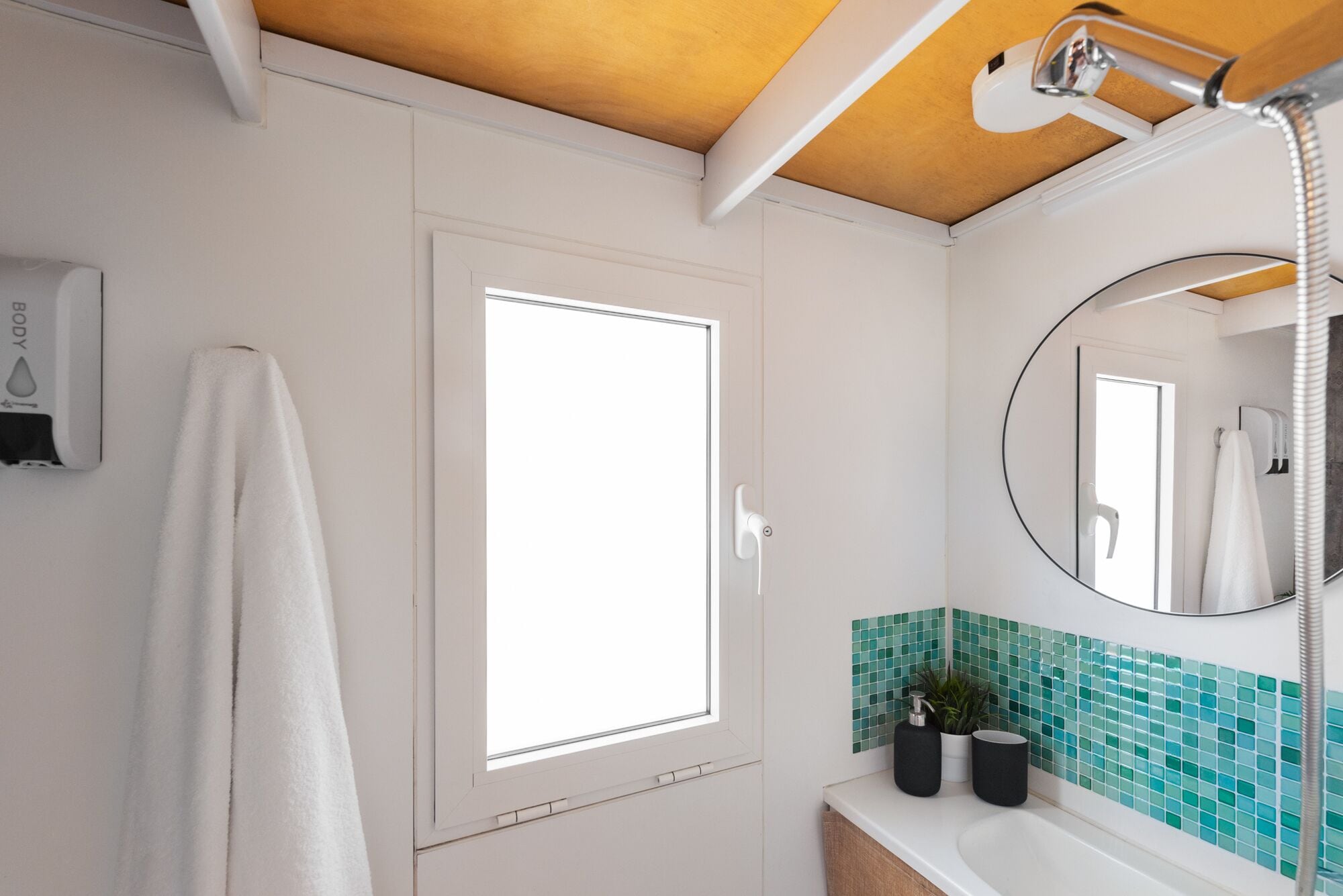 A bathroom with a white door, a window, a mirror, and a sink with a green-tiled backsplash.