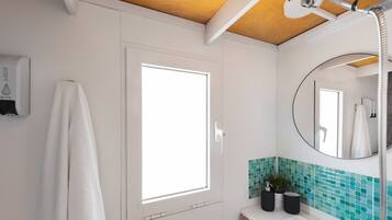 Un baño con una puerta blanca, una ventana, un espejo y un lavamanos con salpicadero de azulejos verdes.