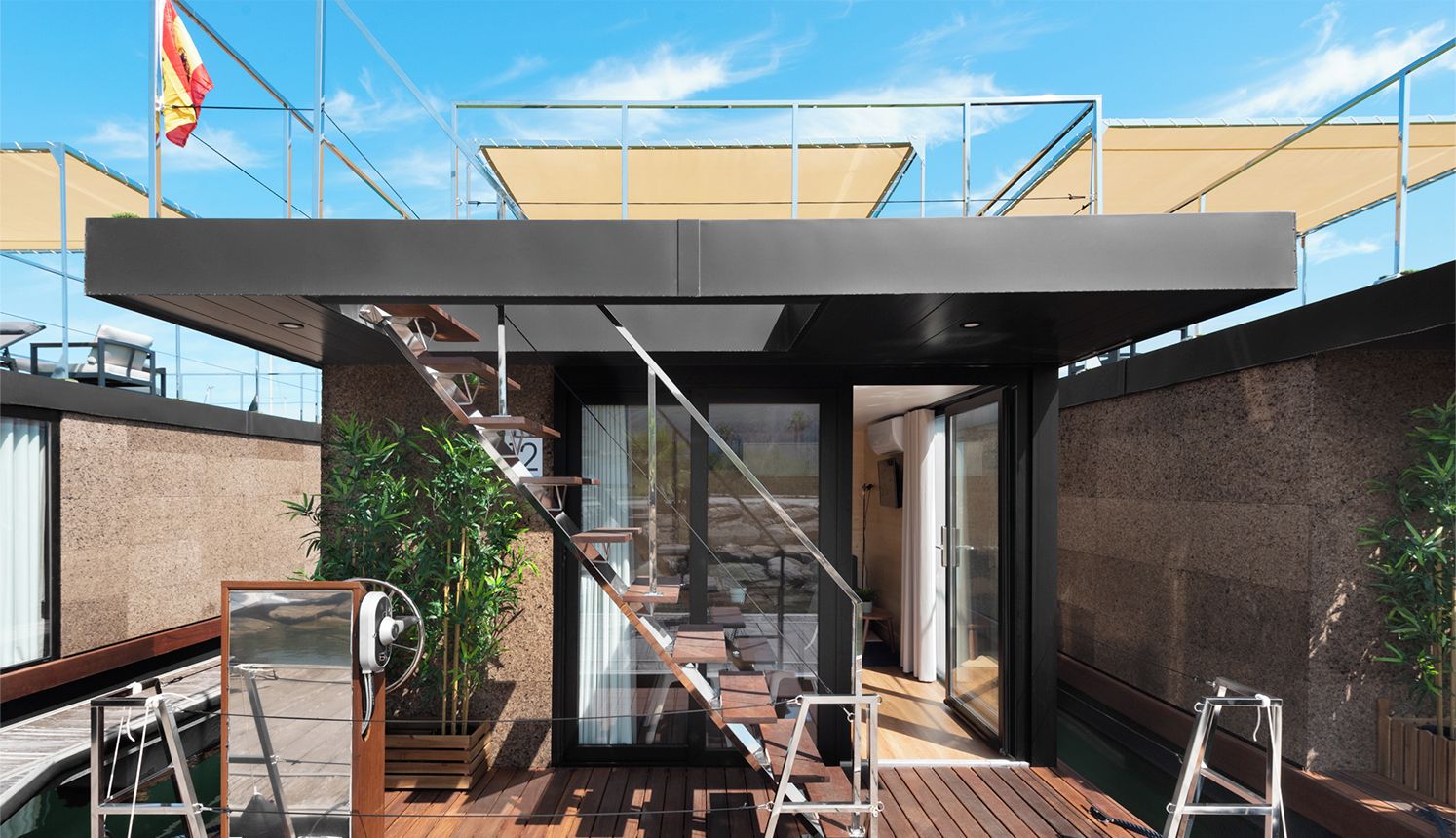 Una moderna casa de barcos con terraza de madera, una escalera que lleva a una puerta de cristal y una bandera al fondo.