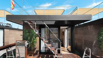 Una moderna casa de barcos con terraza de madera, una escalera que lleva a una puerta de cristal y una bandera al fondo.