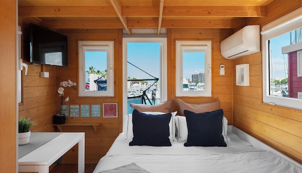 A compact boat house with a bed, a small table, and a TV.