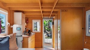 A compact, wooden interior of a boat house with a kitchenette, a bed, and a view of an outdoor area with rocks and greenery. - Boat Haus Mediterranean Experience Alcaidesa  La Linea (La Línea de la Concepción)