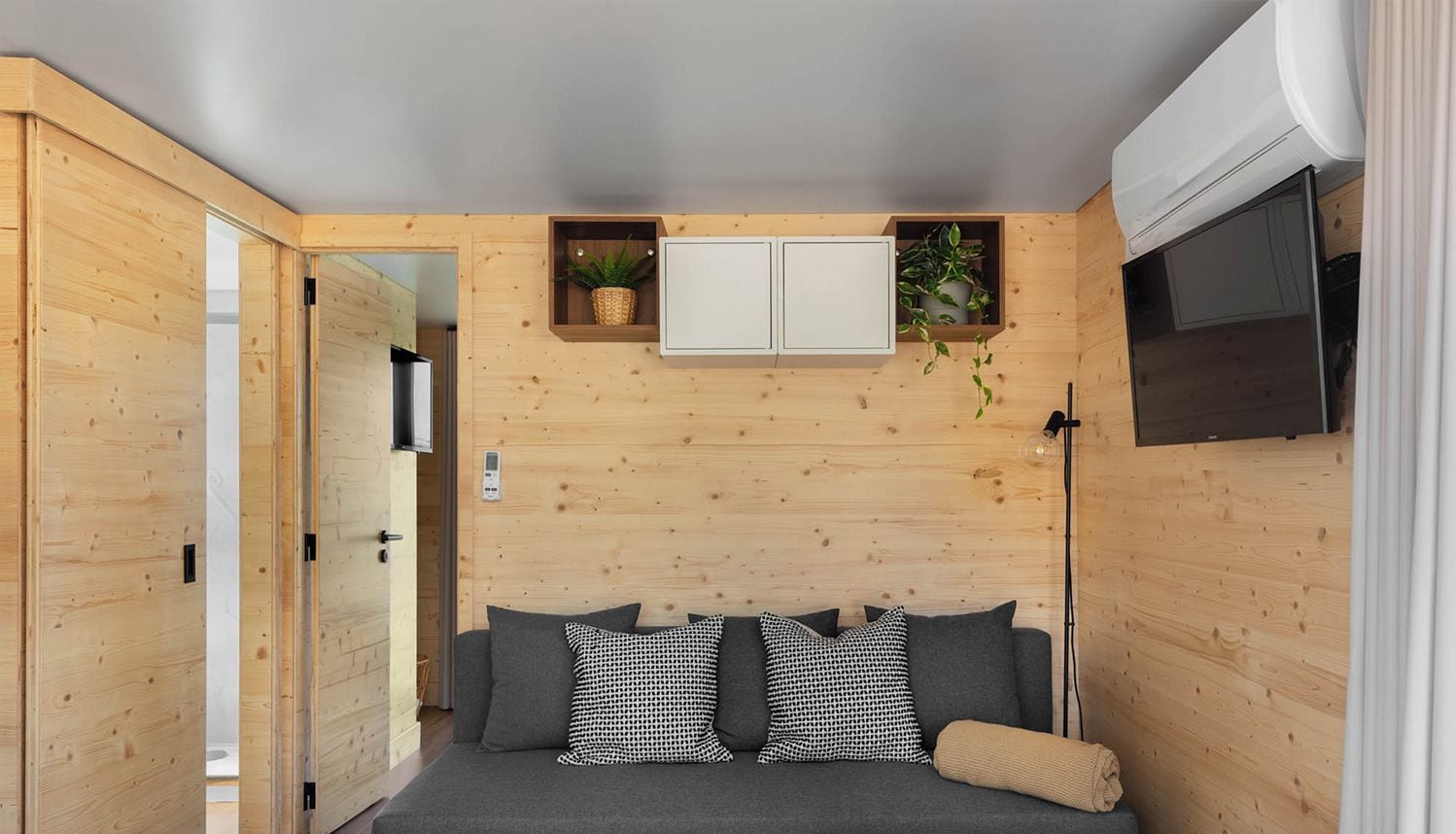 A modern boat house interior with a grey sofa, wooden walls, and a mounted TV.
