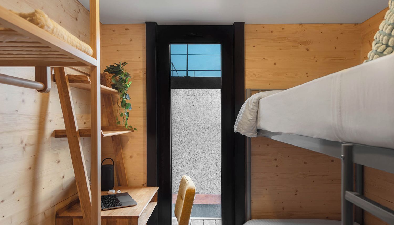 Una habitación pequeña con una cama litera, un escritorio con una computadora portátil, una silla y una planta pequeña.
