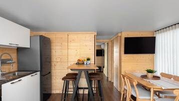 A compact boat house with a kitchen, dining area, and a TV mounted on the wall.