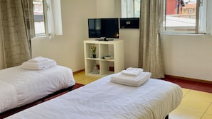 A hotel room with two beds, a TV on a white stand, a small shelf with a Buddha statue, and a window with curtains. - BNBOOK-BORROMEO 2 RHO (RHO)