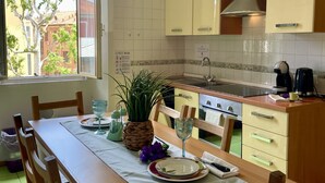 A kitchen with a dining table set for two, a window with a view of buildings, and a plant on the table. - BNBOOK-BORROMEO 2 RHO (RHO)
