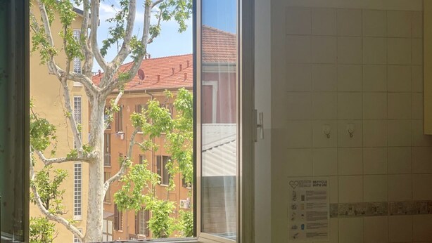 A room with a window overlooking a building with red tiles and a tree in front. - BNBOOK-BORROMEO 2 RHO (RHO)