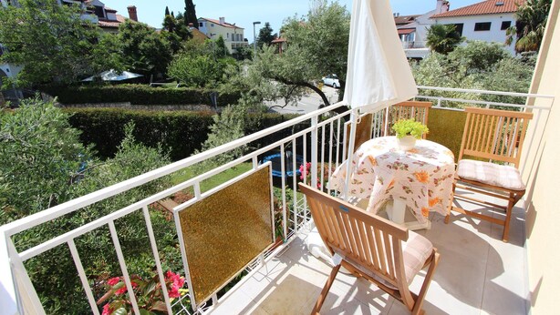 A balcony with a table and chairs, surrounded by a white railing, overlooking a garden and neighboring houses. - ROKOV Two-Bedroom Apartment (Rovinj)