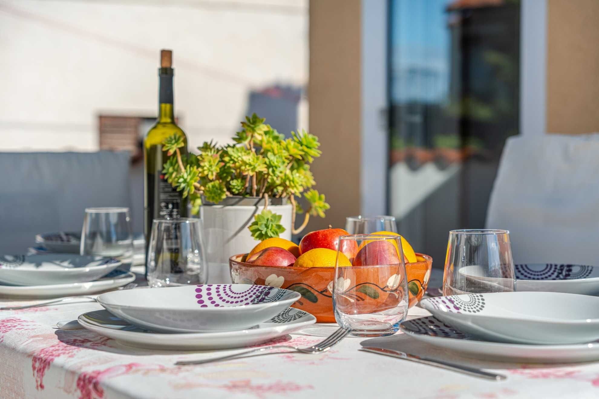 A table set with plates, cutlery, and a fruit bowl with apples and oranges.