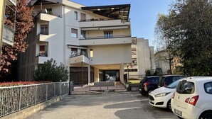 A multi-story residential building with balconies, a covered entrance, and a parking area with cars.