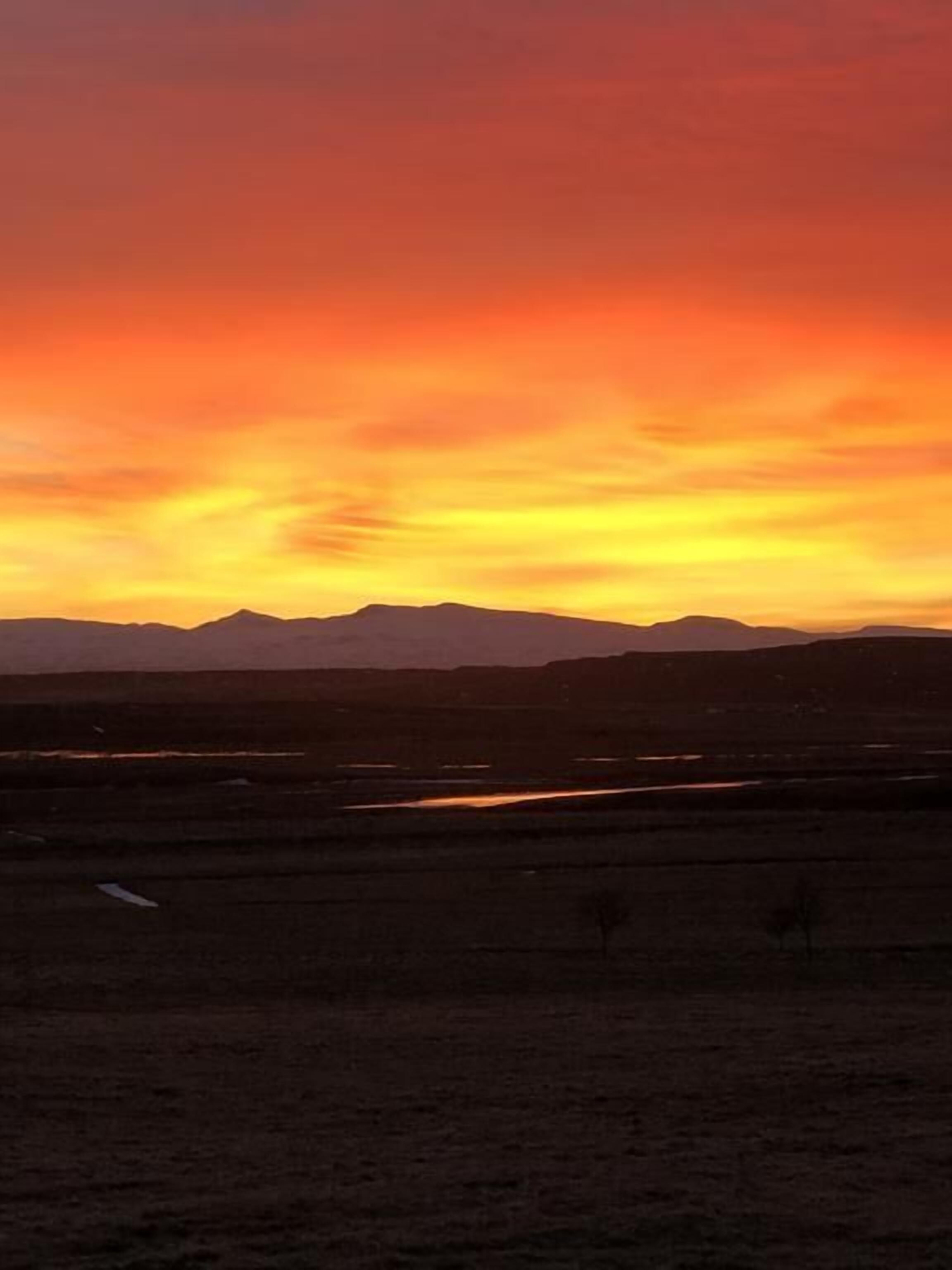 A flat landscape with distant mountains and a sunset sky.