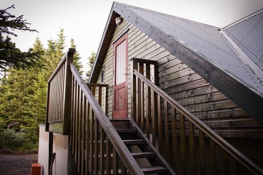 Eine Holzhütte mit einer Treppe, die zu einer Tür führt, umgeben von Bäumen.
