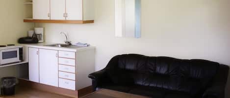 Un espacio habitable compacto con kitchenette, un sofá de cuero negro y una mesa de centro de madera.