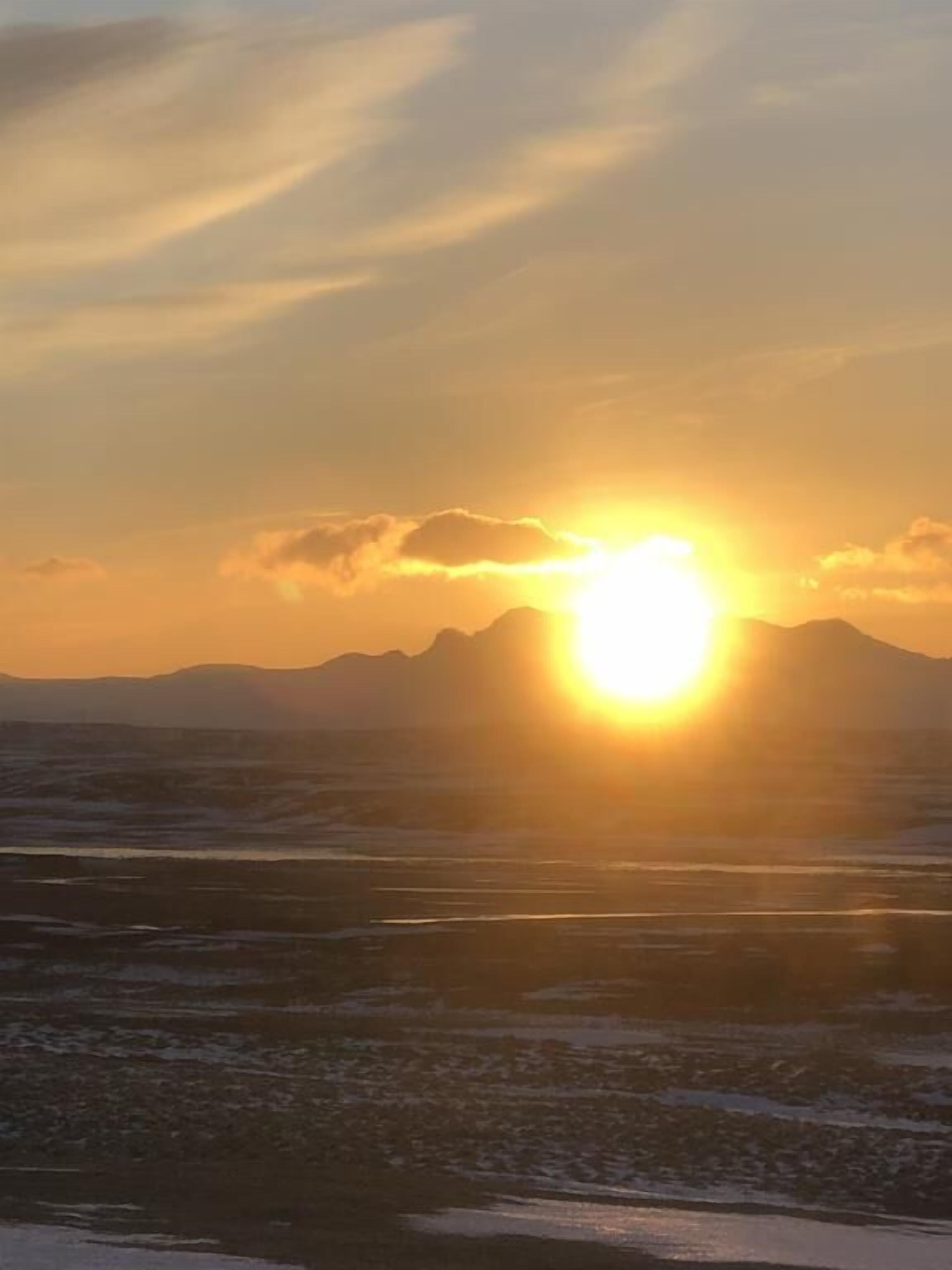 Un atardecer sobre un paisaje montañoso con una masa de agua al frente.