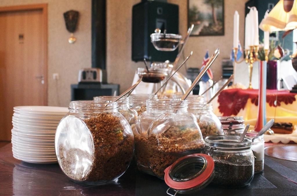 Uma mesa com vários potes de vidro contendo alimentos, uma pilha de pratos brancos e um castiçal com velas.