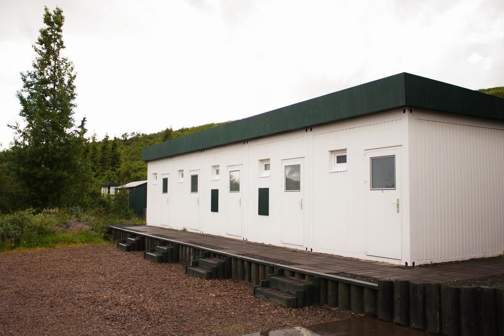 A white building with a green roof, multiple windows, and a wooden deck leading to the entrance.