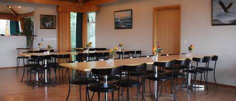 A spacious dining area with wooden tables and black chairs, featuring a wooden ceiling and framed artwork on the walls.